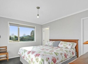 Ein Schlafzimmer mit großem Fenster, einem Bett mit floralem Bettzeug, einem Holz-Kopfteil und einer kleinen Holzbank.