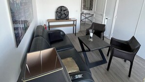 A modern living room with a sectional sofa, a standing fan, a coffee table, and a dining area with chairs.