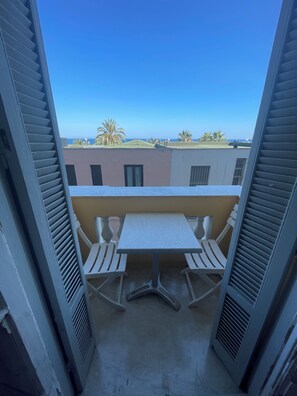 A balcony with a table and chairs, overlooking a residential area with palm trees and a clear sky.