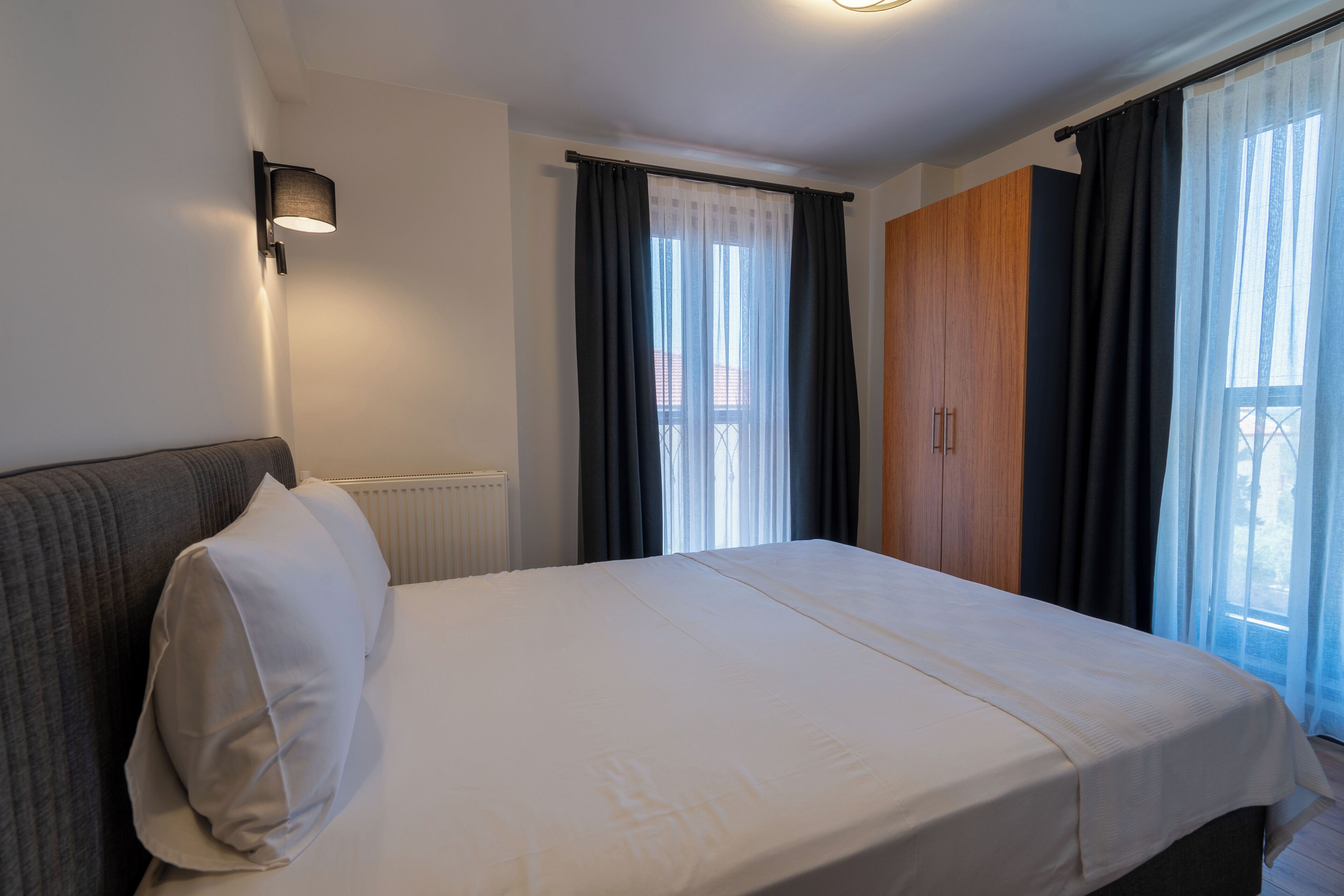 Cama bem arrumada em quarto de hotel, com vista para o exterior através de uma janela com cortinas leves.