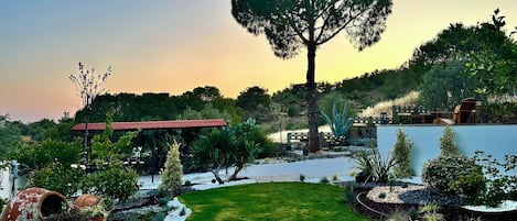 A well-maintained garden with a large tree, a gazebo, and a variety of plants.