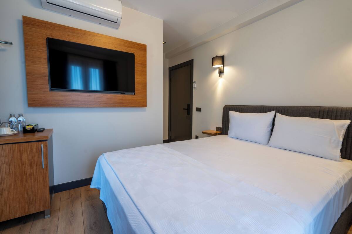 Habitación de hotel con una cama grande, un aparador de madera, un televisor montado y una lámpara fijada a la pared.
