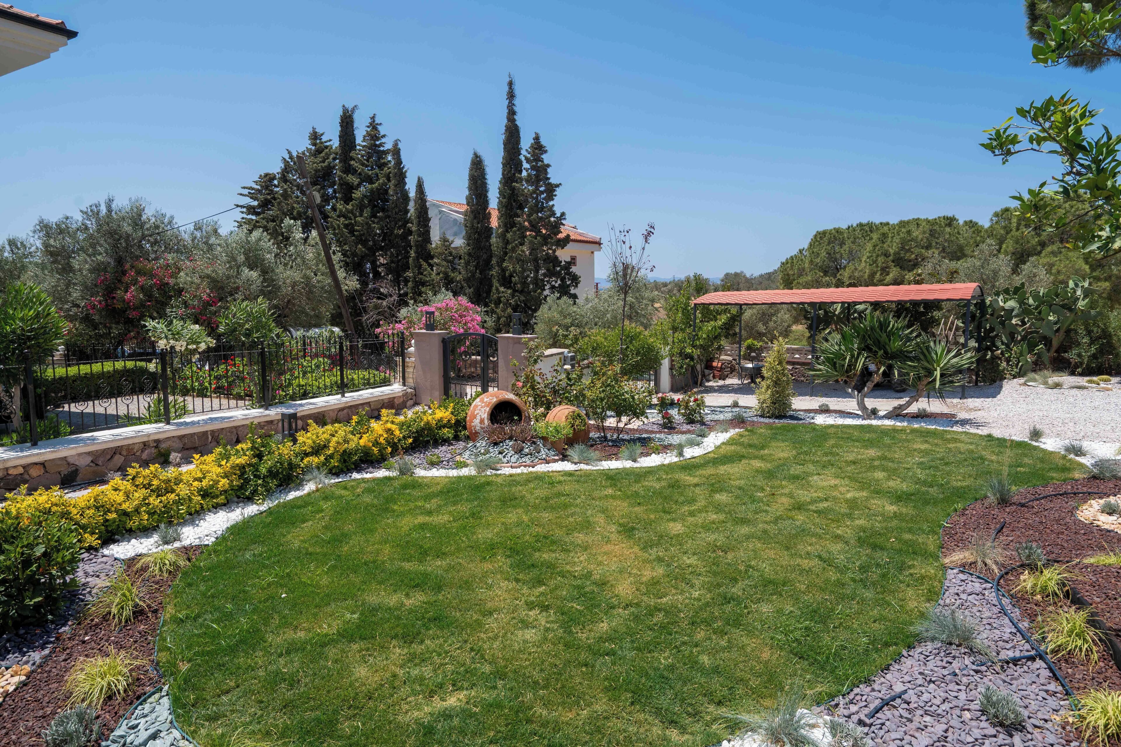 Un jardí ben cuidat amb gespa, diverses plantes i una estructura de pergola.