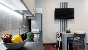 A modern kitchen with a built-in stove, a sink, and a bowl of colorful bell peppers. There is a dining area with a table and chairs, and a flat-screen TV mounted on the wall. - The Little Etruscan, cozy tourist rental in the center of Arezzo (Arezzo)
