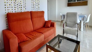 A modern living room with a red sofa, a glass coffee table, and a TV mounted on the wall. - Apartment in Spain by the Sandy Beach (Torroella de Montgrí)