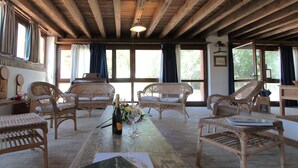 Ein geräumiges Zimmer mit hohen Holzbalkendecken, Korbmöbeln und großen Fenstern mit Blick auf Grünflächen.