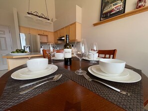 A dining table set with white plates, bowls, cutlery, and wine glasses, with a bottle of wine in the center.