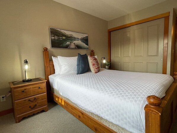 A bedroom with a wooden bed, a nightstand, a lamp, and a painting on the wall.