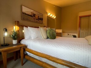 A bedroom with a bed, bedside table, lamp, and a painting on the wall.