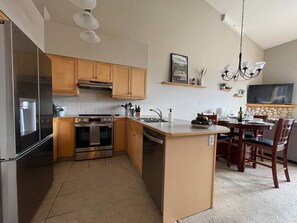A modern kitchen with stainless steel appliances, wooden cabinets, and a dining area with a stone fireplace.