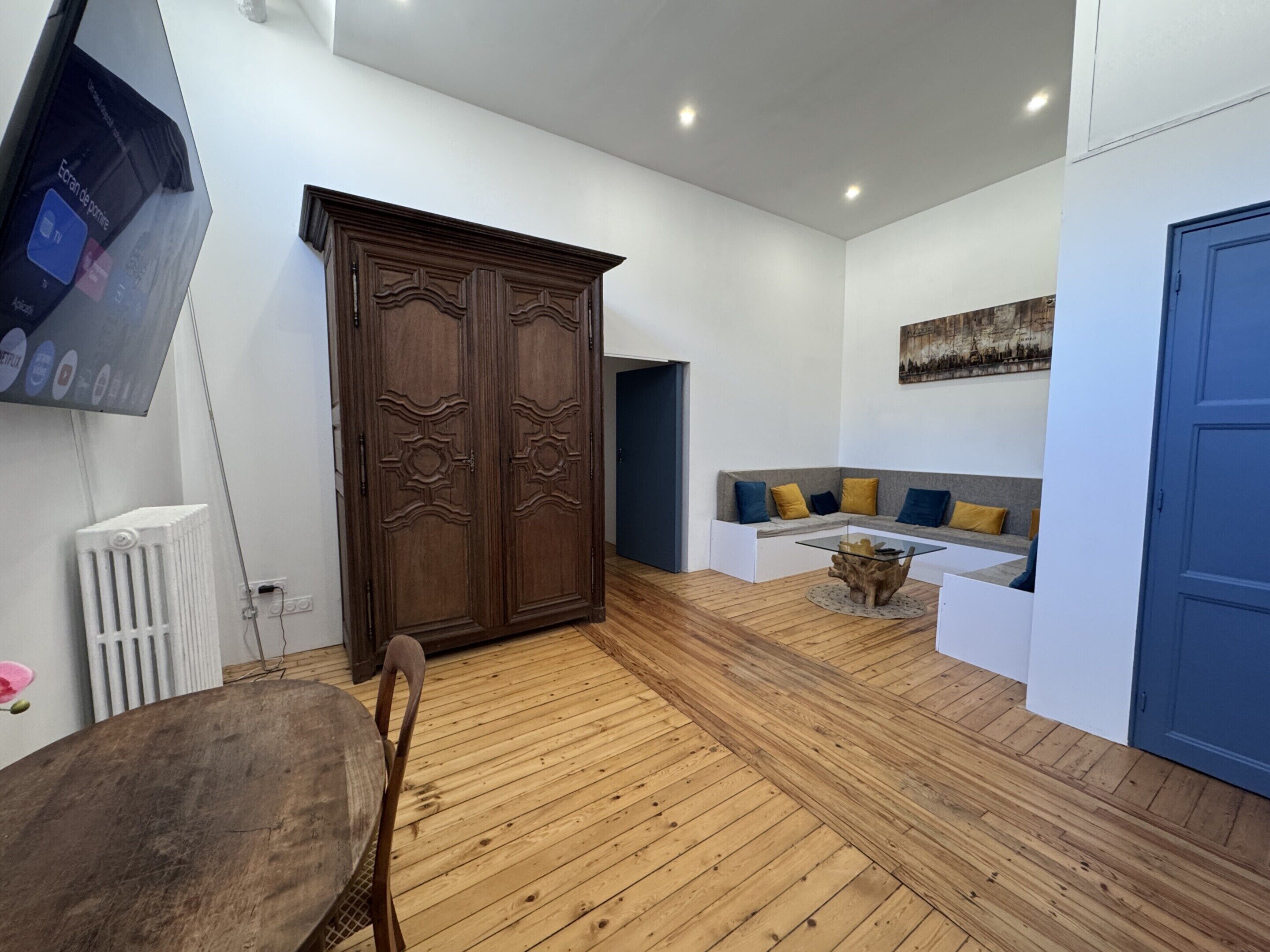 Uma sala de estar moderna com piso de madeira, um guarda-roupa grande, um espaço de estar com almofadas e uma televisão fixada na parede.