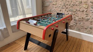 Una mesa de fútbolín en una habitación con suelo de madera y pared de piedra.