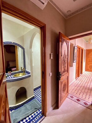 A hallway with a tiled floor, a wooden door with intricate carvings, and a mirror with a blue and white tile border. - Riad Rose Mati (Marrakech)