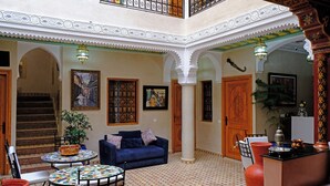 A spacious interior with a high ceiling, a blue sofa, a patterned table, and a staircase leading to an upper level. - Riad Rose Mati (Marrakech)