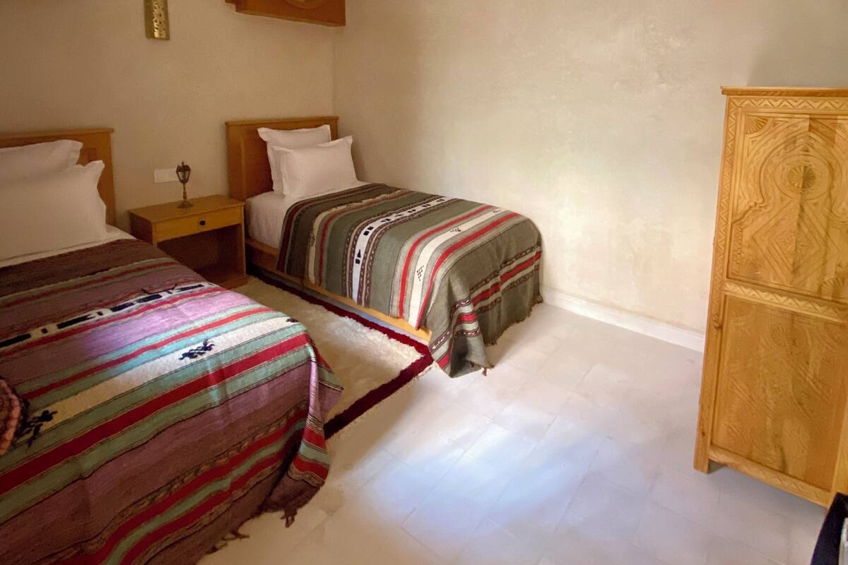 A bedroom with two beds, a wooden wardrobe, and a decorative ceiling light.