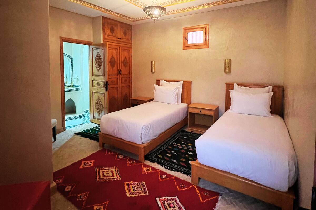 A hotel room with two beds, a red patterned rug, wooden headboards, and a decorative ceiling.