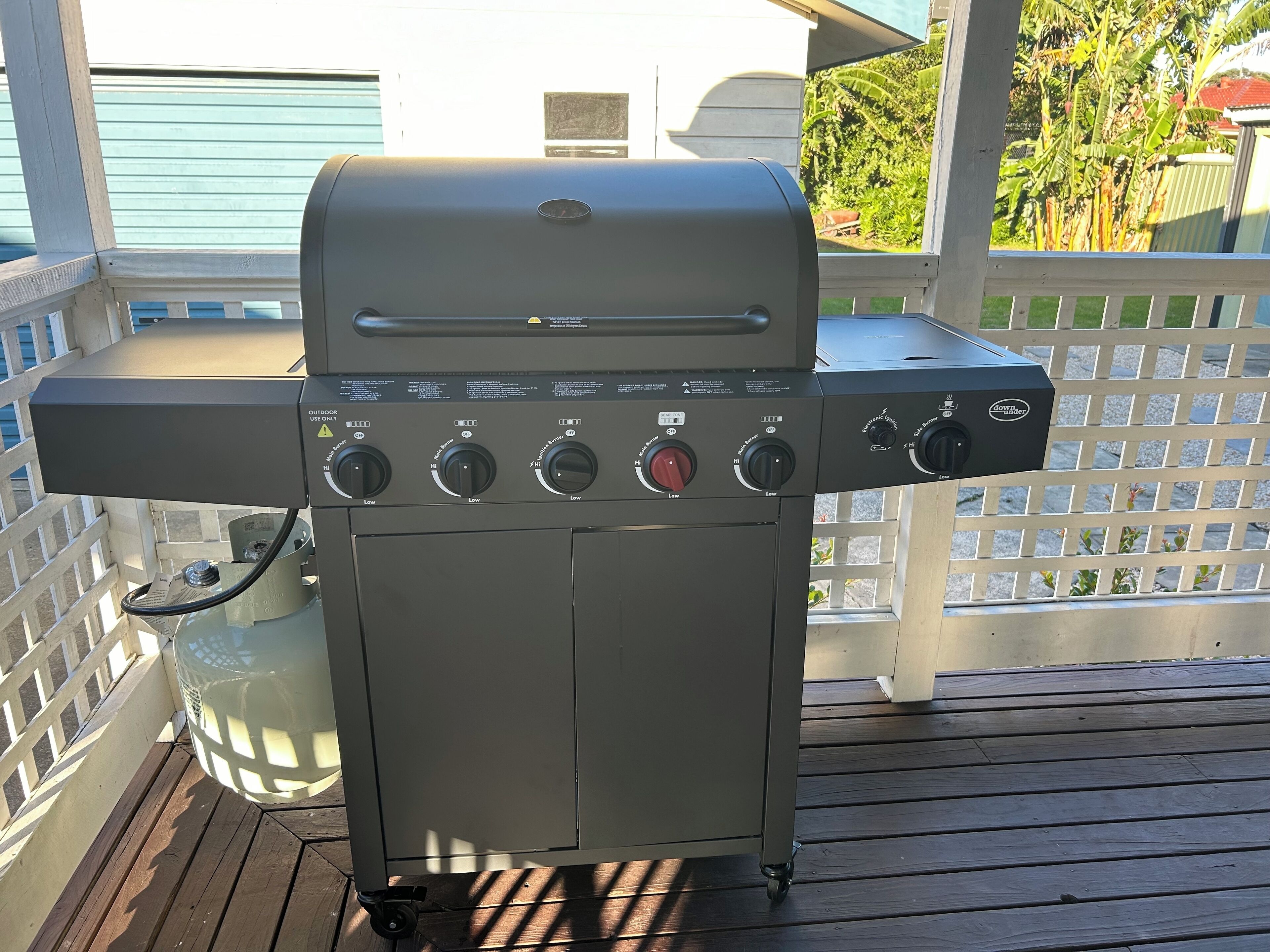 Een barbecue op een terras met een wit hek en vrij uitzicht op de achtertuin.