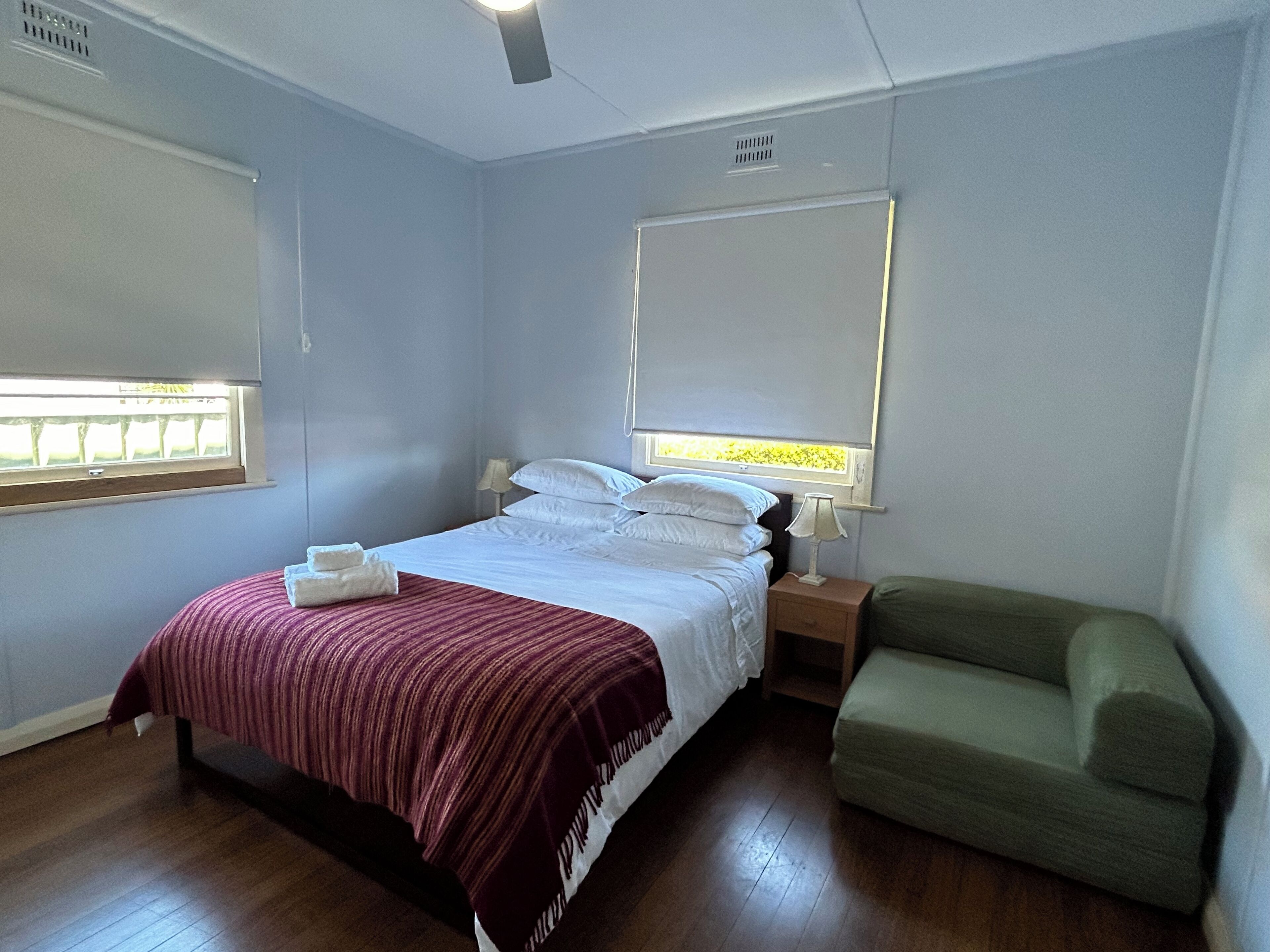 A bedroom with a bed, bedside tables, a nightstand, a green armchair, and a window with blinds.