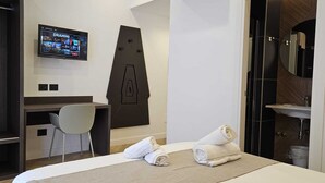 Een hotelkamer met een bed, een bureau, een stoel, een tv die een zender toont, en een spiegel.