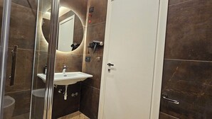 Een moderne badkamer met een douchecabine van glas, een witte wastafel en een grote spiegel.