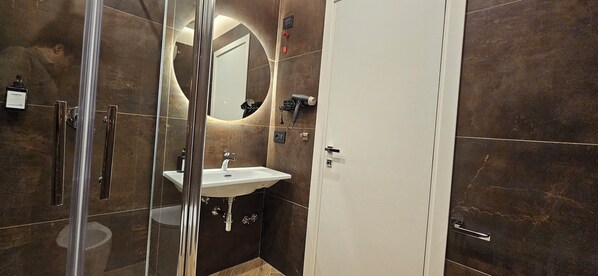 A modern bathroom with a glass shower enclosure, a white sink, and a large mirror.