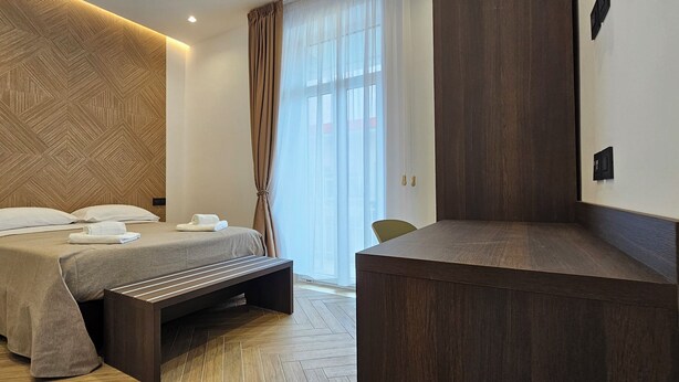 Een moderne hotelkamer met een bed, een bankje en een bureau.