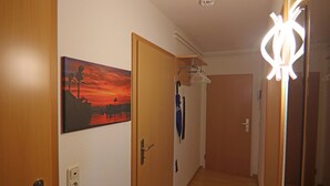 Un couloir avec des portes en bois, un tableau représentant un coucher de soleil et un porte-manteau sur lequel est accroché un vêtement bleu.