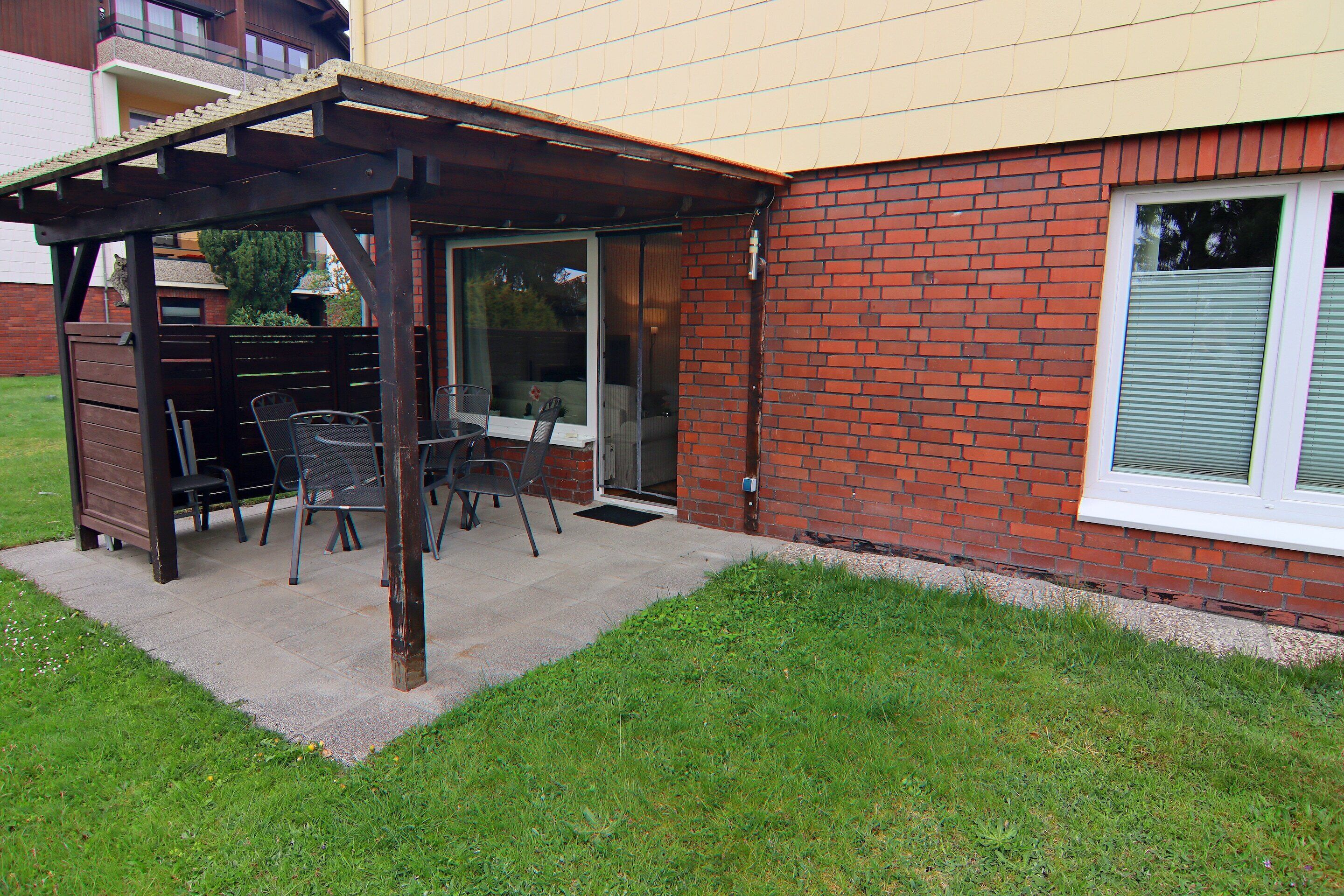 Un patio con pérgola, mobiliario exterior y pared de ladrillo.