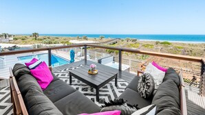 A balcony with a pool, outdoor seating, and a view of the beach. - Luxury Ocean Front, Near Downtown, Heated Pool, Hot Tub, Game Room, Sleeps 28 (St. Augustine)