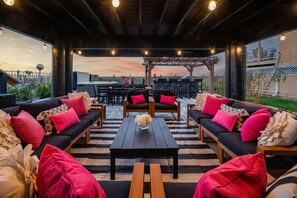Une terrasse extérieure aménagée avec des canapés, des fauteuils et une table, offrant une vue sur le ciel et un bâtiment en arrière-plan.