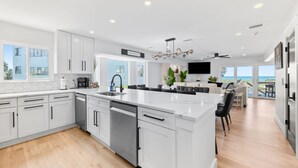 A modern kitchen with white cabinetry, a central island, and a large window overlooking the ocean. - Luxury Ocean Front, Near Downtown, Heated Pool, Hot Tub, Game Room, Sleeps 28 (St. Augustine)