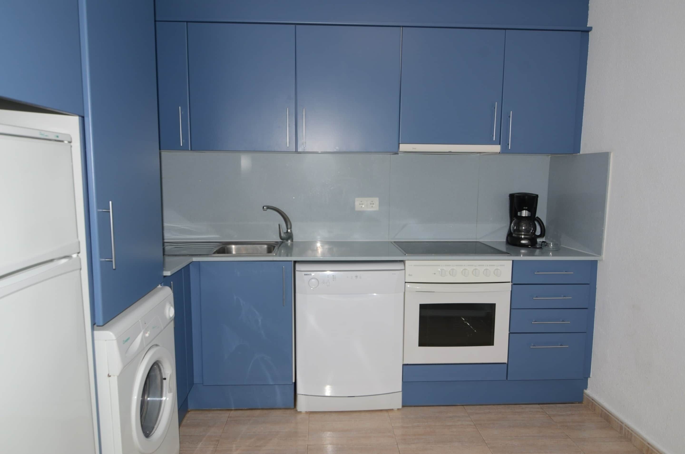 A compact kitchen with blue cabinets, a washing machine, a dishwasher, and a coffee maker.