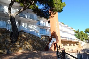 Un edificio de varios pisos con balcones, un muro de piedra y una escalera que conduce a la entrada.