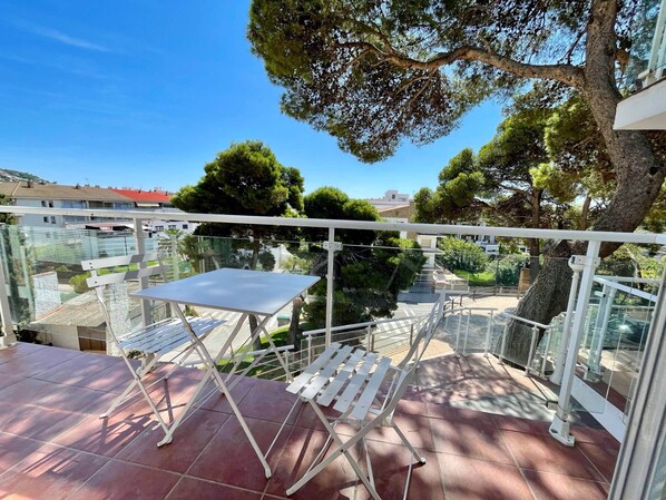 Ein Balkon mit Tisch und zwei Stühlen, mit Blick auf ein Wohngebiet mit Bäumen und Häusern.