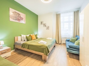 Une chambre à coucher avec un lit, une table de chevet, un canapé bleu et une fenêtre avec des rideaux.