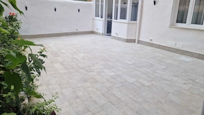 Un espace patio ouvert avec un sol carrelé, des murs blancs et de grandes fenêtres.