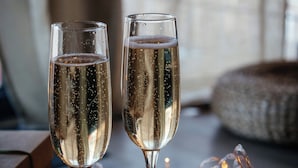 Two champagne flutes on a wooden surface with string lights and dark round objects, possibly chocolates, in a dimly lit setting. - Cosy nest in SAINT VALERY EN CAUX near the sea. (Saint-Valery-en-Caux)