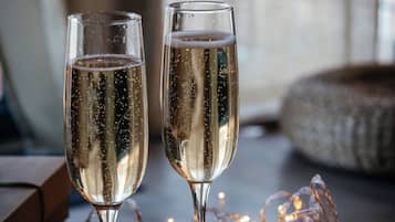 Two champagne flutes on a wooden surface with string lights and dark round objects, possibly chocolates, in a dimly lit setting.