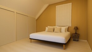 A bedroom with a bed, a nightstand, a lamp, and a large window with a view. - Cosy nest in SAINT VALERY EN CAUX near the sea. (Saint-Valery-en-Caux)