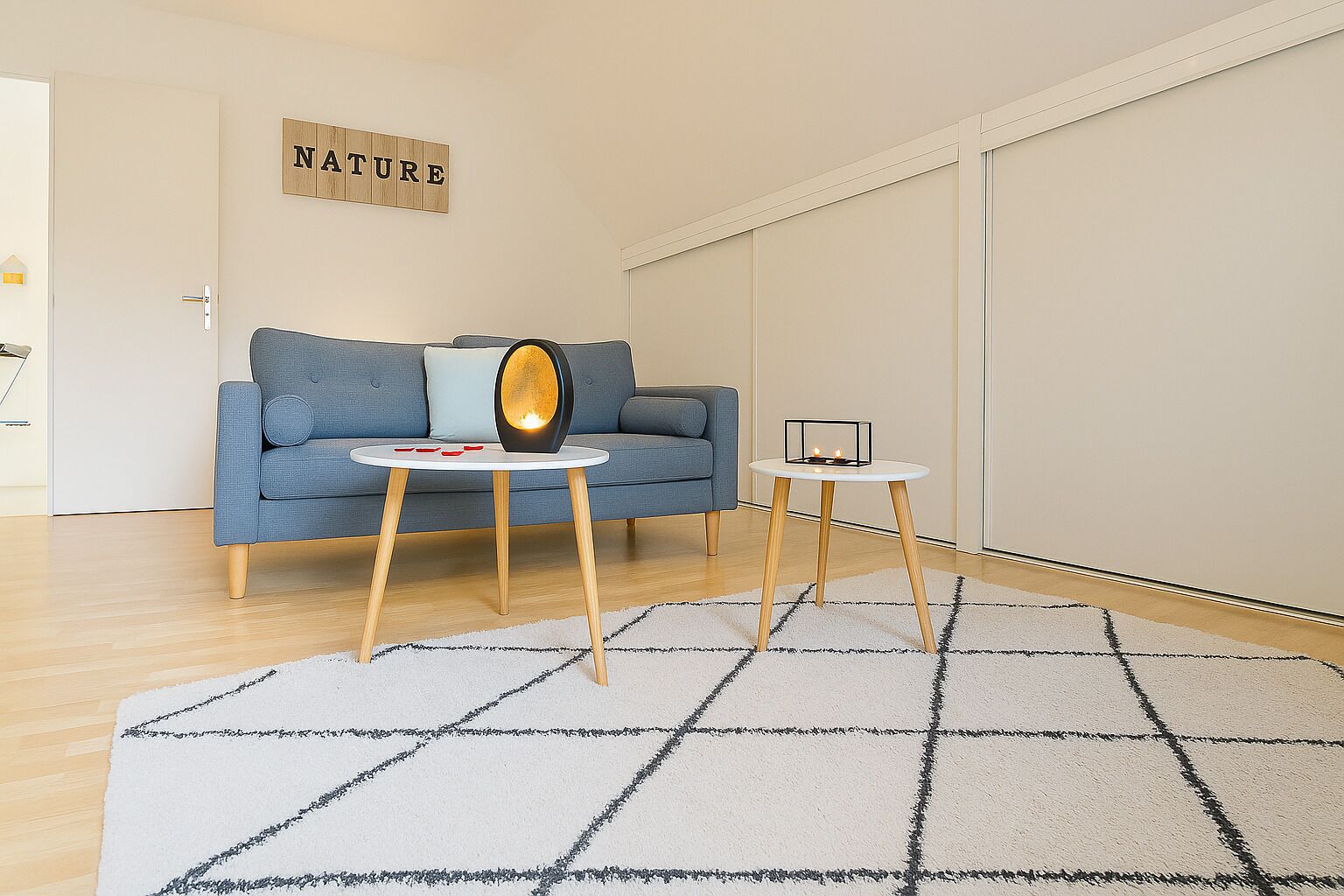 Ein modernes Wohnzimmer mit einem blauen Sofa, einem runden Tisch mit Kerze und einem Teppich mit geometrischem Muster.