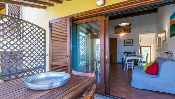 A wooden table with a metal bowl, a wooden chair, and a glass door leading to a dining area with a table and chairs. - Cosy apartment for 5 guests with WIFI, A/C, terrace and pets allowed (Guardistallo)