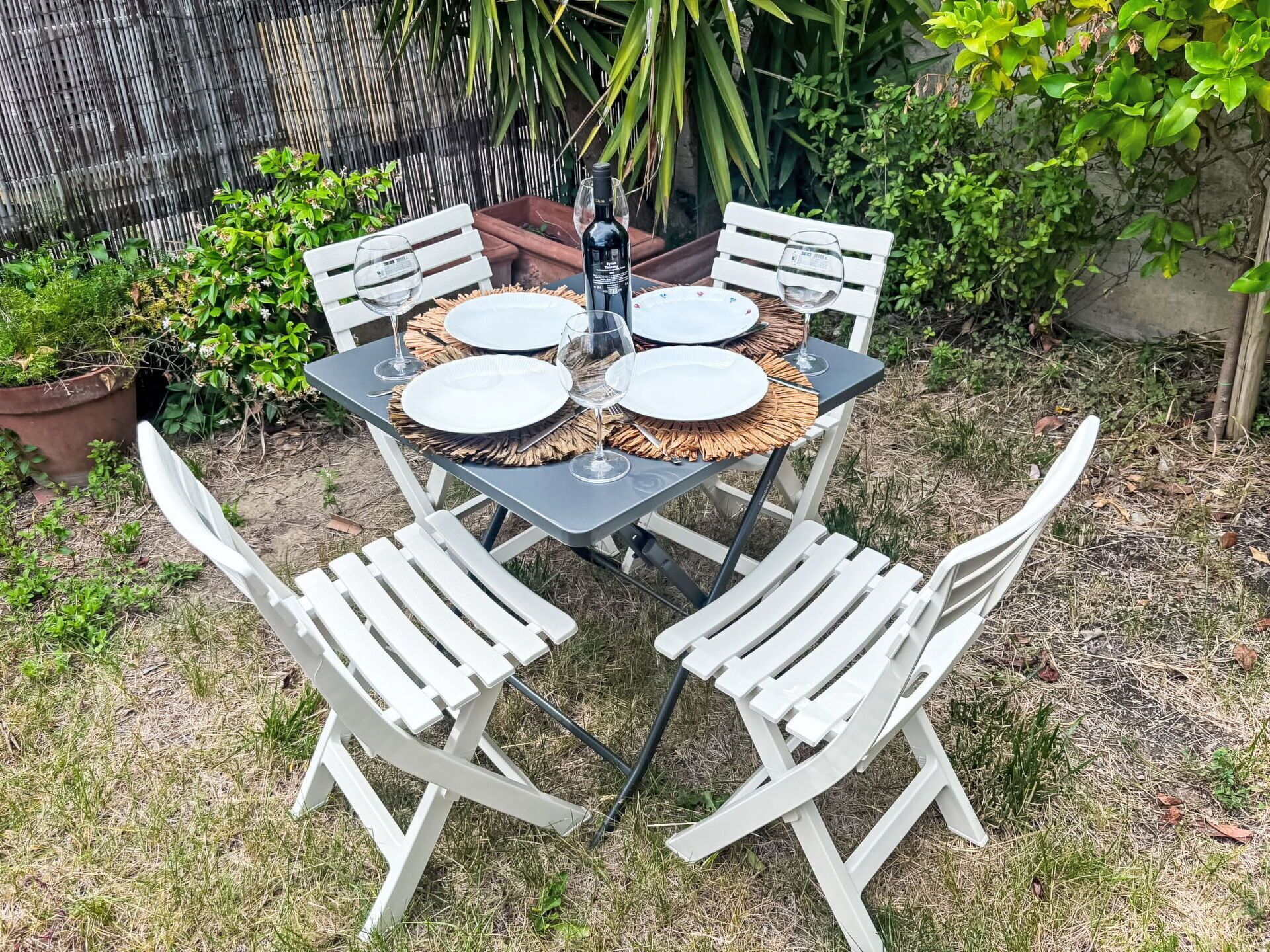 Une table dressée à l’extérieur, avec des chaises blanches, une bouteille et des verres.