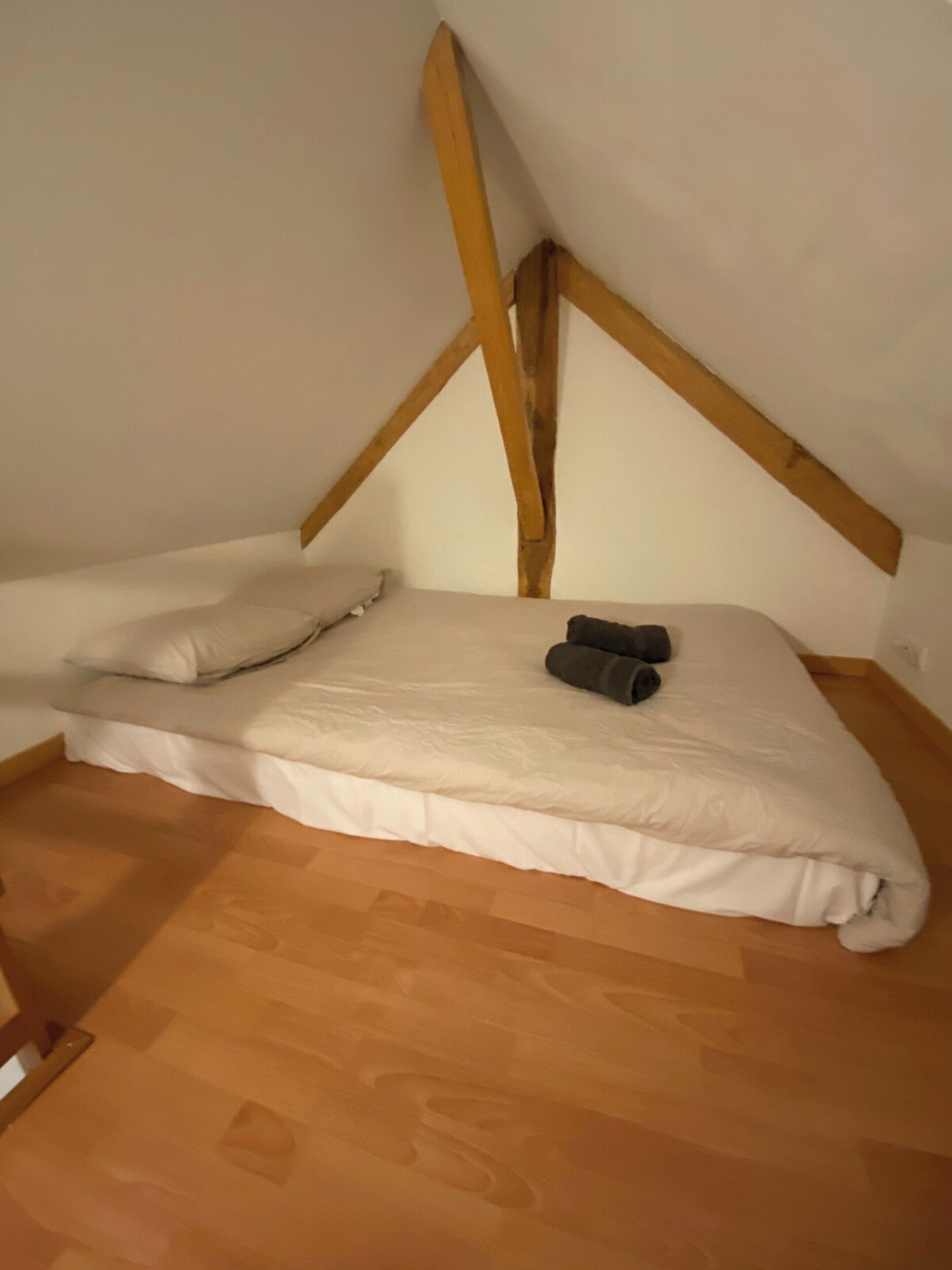 Een enkel bed in een kamer met houten balken aan het plafond, een wit matras en een kussen.