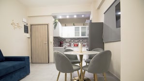 Een compacte woonruimte met een eethoek, bestaande uit een ronde tafel en vier stoelen, een blauwe bank en een keuken met witte kastjes en een rode inrichting.