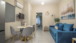 Een moderne woonkamer met een blauwe bank, een eettafel met stoelen, een flatscreen televisie en een airconditioner.