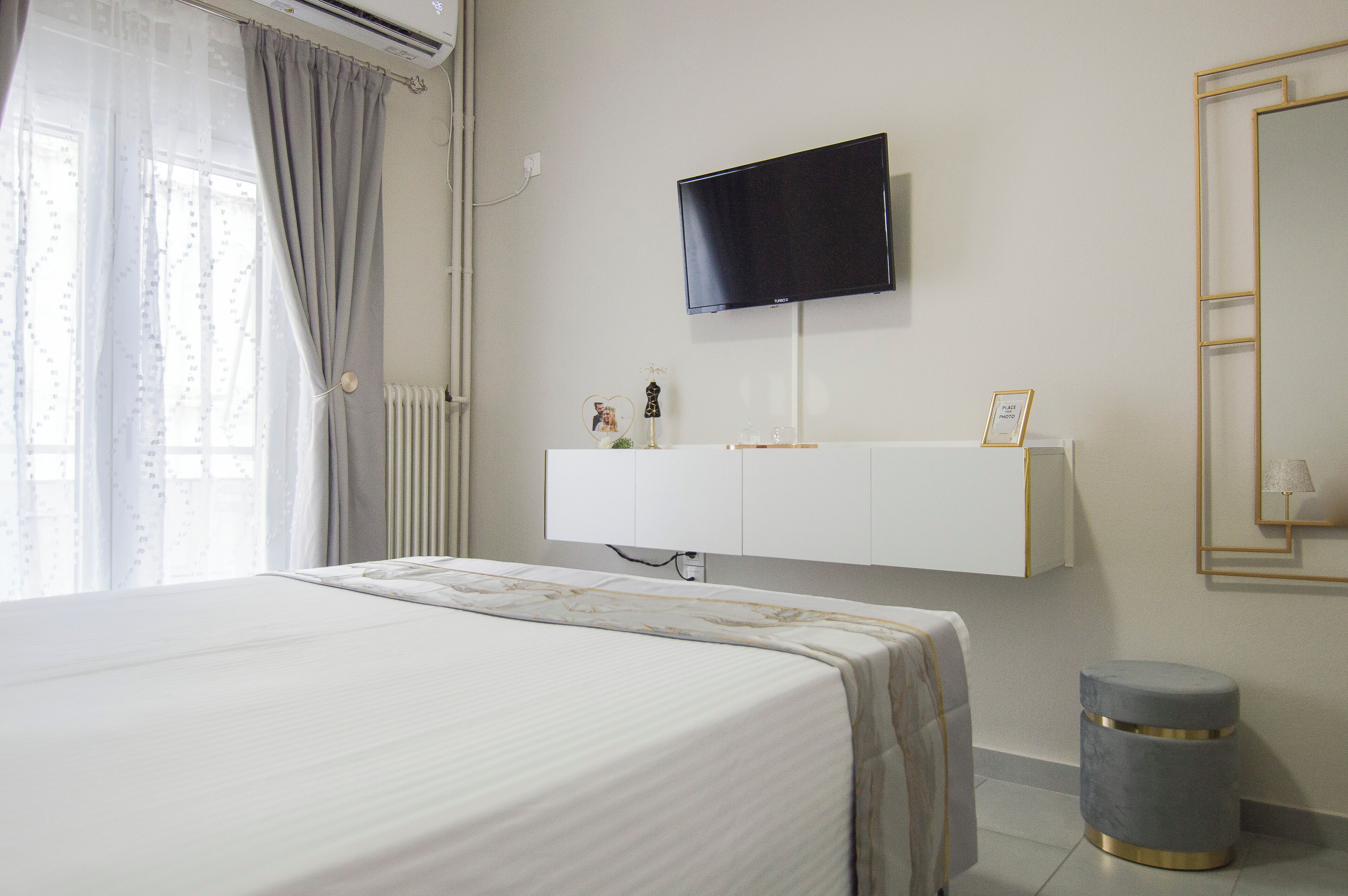 Une chambre d’hôtel avec un lit, un téléviseur fixé au mur, un radiateur et un petit tabouret rond.