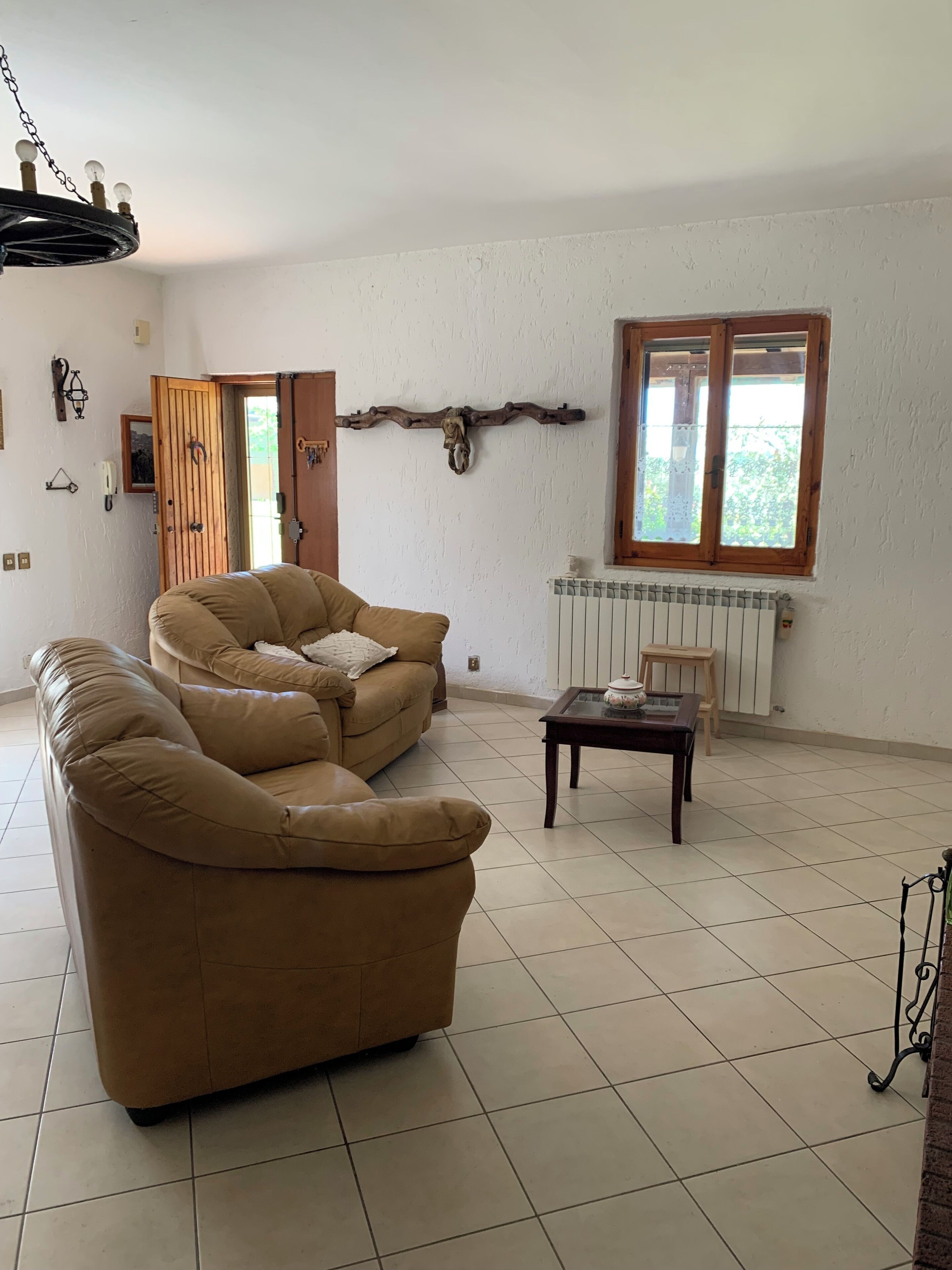 Een woonkamer met een beige bank, een houten salontafel, een radiator en een houten kruis aan de muur.