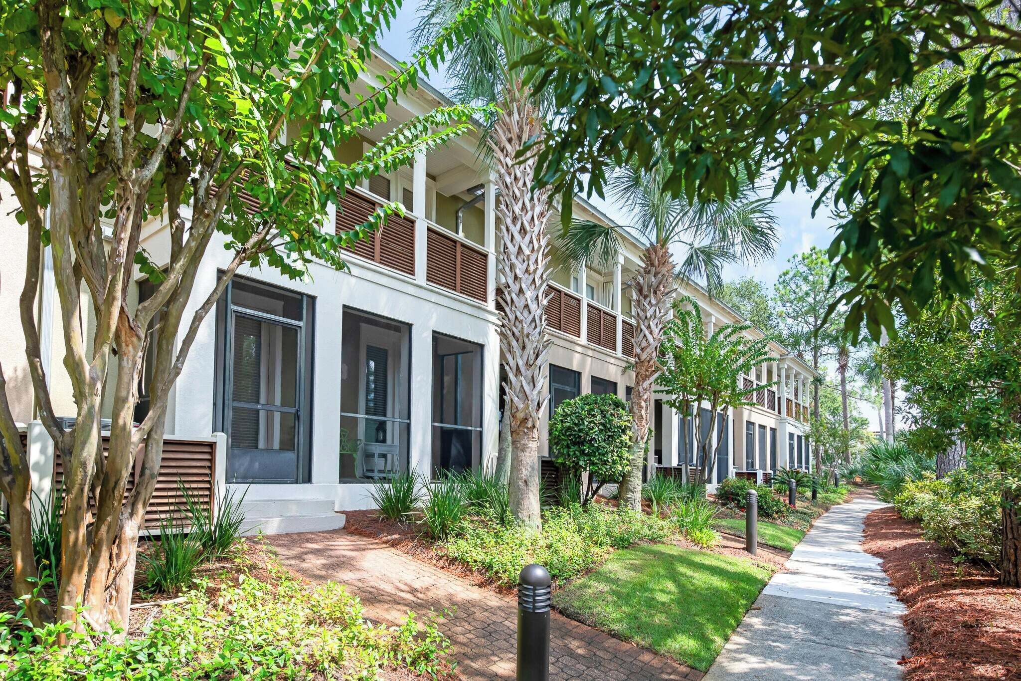 A modern building with large windows, a paved pathway, and lush greenery.