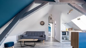 A loft-style living space with a gray sofa, a wooden coffee table, and a kitchenette area. - Chic Apartment Near City Center (Ecommoy)