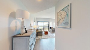 A modern living room with a large window, a map on the wall, and a lamp on a console table.